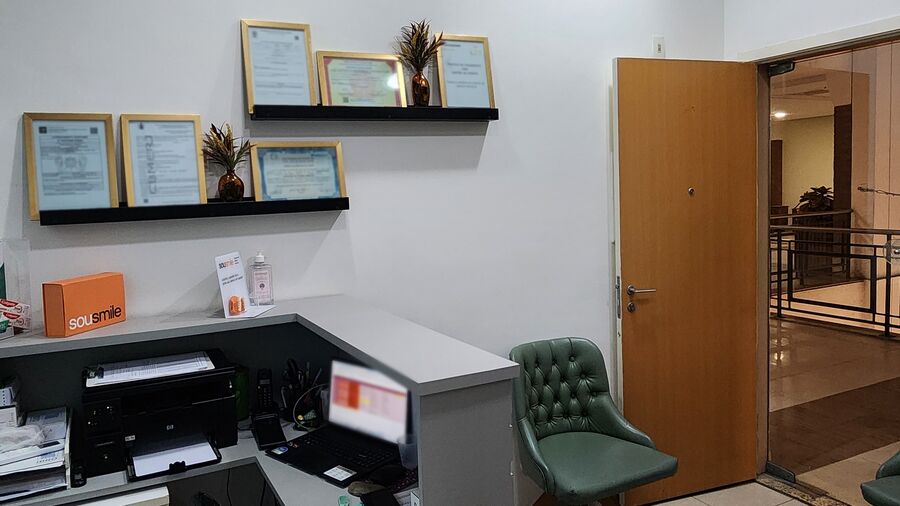Recepção da Litz: o balcão, certificados emoldurados na parede, uma poltrona verde capitonê e a porta de entrada
