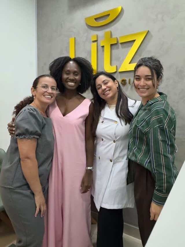 Quatro integrantes da equipe Litz sorrindo juntos em frente ao letreiro dourado da clínica
